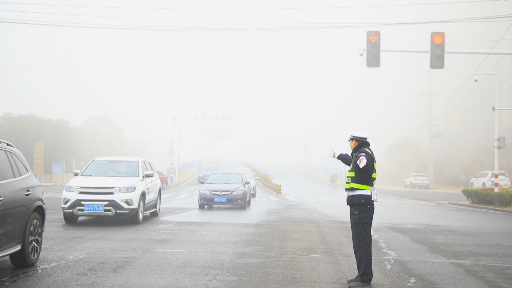 圖為執(zhí)勤民警正在大霧中指揮過往車輛有序通行.jpg